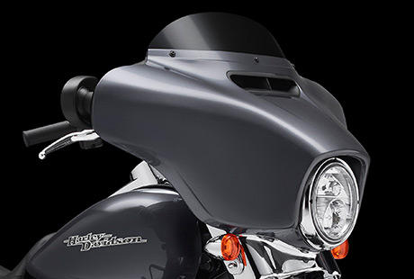 Street Glide / Neu gestaltete Verkleidung reduziert Verwirbelungen:    Um dem Fahrtwind Paroli zu bieten, zog Harley-Davidson alle Register: Strmungsmechanik und komplizierte Algorithmen auf Supercomputern sowie die Rckmeldungen von unzhligen Windkanaltests mit Fahrern im Sattel. Danach ging es fr Tausende von Meilen hinaus auf die Strae  mit echtem Fahrtwind, echtem Sturm, echtem Nieselregen und echten Wolkenbrchen. Das Ergebnis: Eine klassische und dennoch vollkommen berarbeitete Batwing Verkleidung, die fr eine sanftere Luftumstrmung sorgt und die Verwirbelungen im Kopfbereich reduziert. Der neue, auf Tastendruck zu ffnende und zu schlieende Luftkanal leistet den grten Beitrag dazu. Das Gefhl im Sattel wird noch besser.
