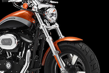 Sportster XL 1200 Custom Limited A / Breite Frontpartie:    Die Frontpartie der Sportster 1200 Custom A fllt dem Betrachter unmittelbar ins Auge. Ihre krftigen Gabelbrcken sind ebenso unverkennbar wie der breite Vorderreifen auf dem schwarzen, teilpolierten fnfspeichigen 16-Zoll-Rad. Schauen Sie genau hin. Was Sie hier sehen, ist der unverflschte Charakter einer echten Sportster, nur einen Touch wuchtiger und mit etwas mehr Custom-Style.
